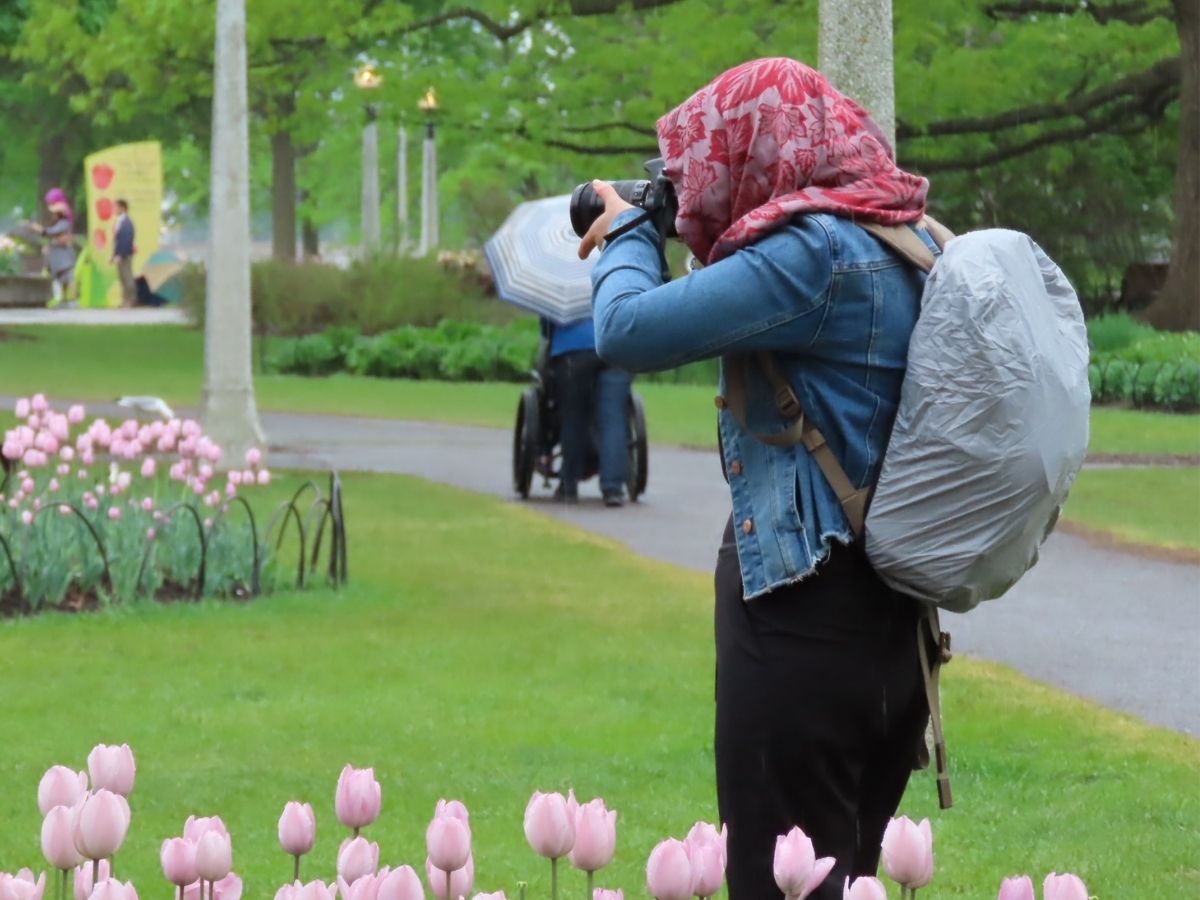 person taking photo in rain, head covered, backpack covered