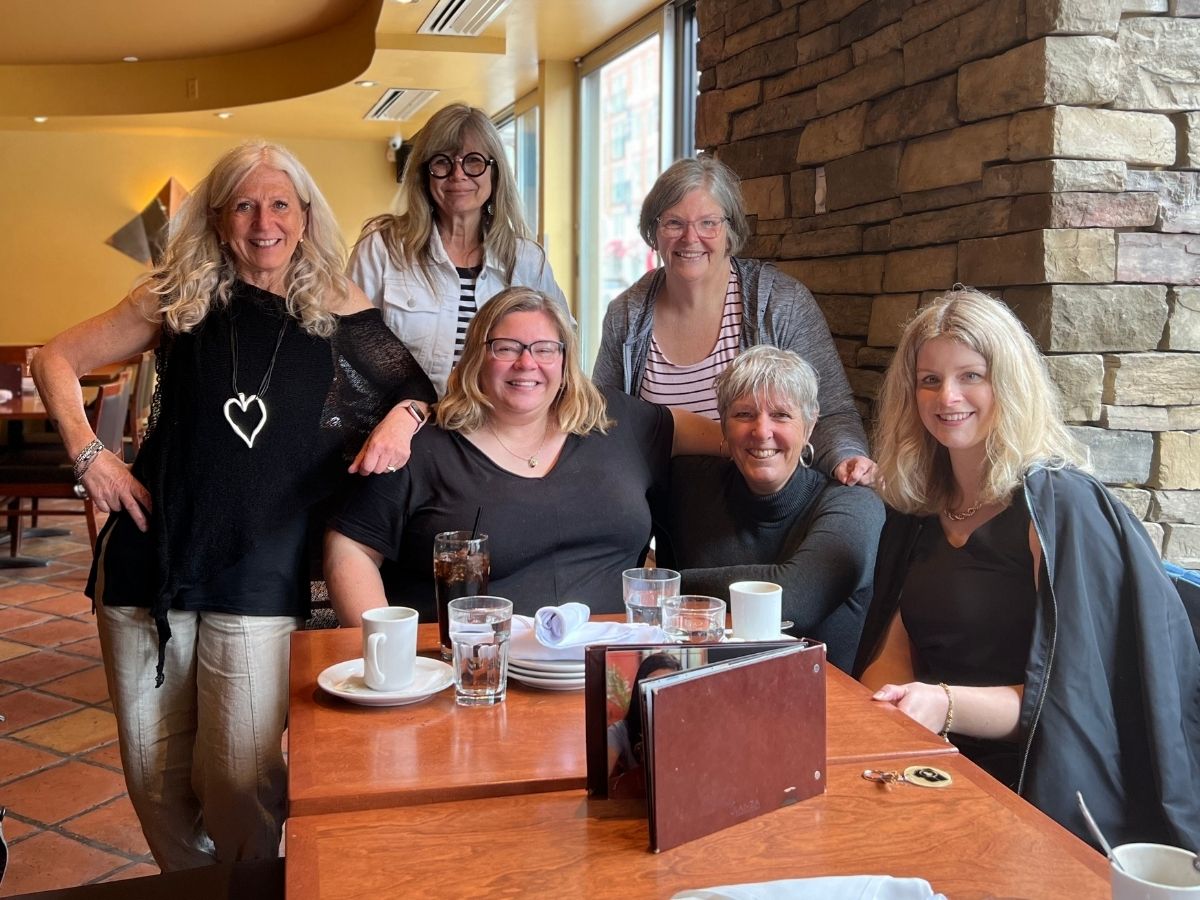 Six women posing together at end of table in restaurant